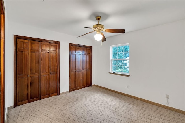 unfurnished bedroom featuring carpet floors, ceiling fan, and multiple closets