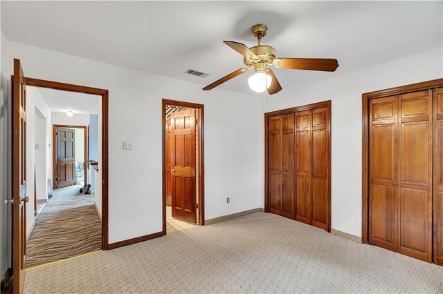 unfurnished bedroom with multiple closets, ceiling fan, and carpet flooring