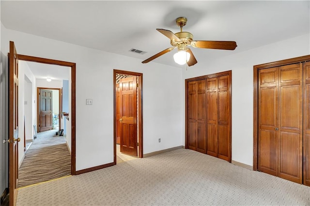 unfurnished bedroom with ceiling fan, two closets, connected bathroom, and light colored carpet