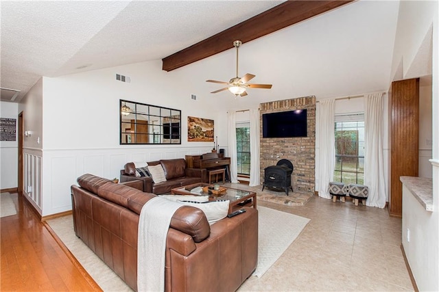 living room featuring lofted ceiling with beams, ceiling fan, a wood stove, and a textured ceiling