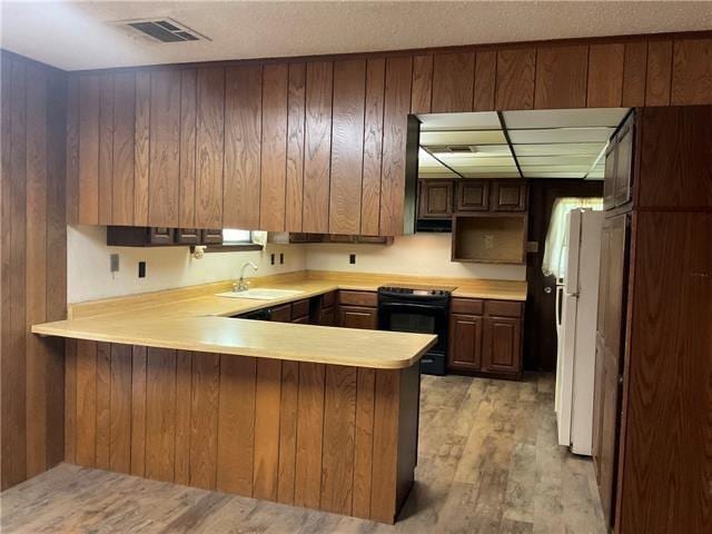 kitchen with sink, light hardwood / wood-style flooring, electric range, white refrigerator, and kitchen peninsula