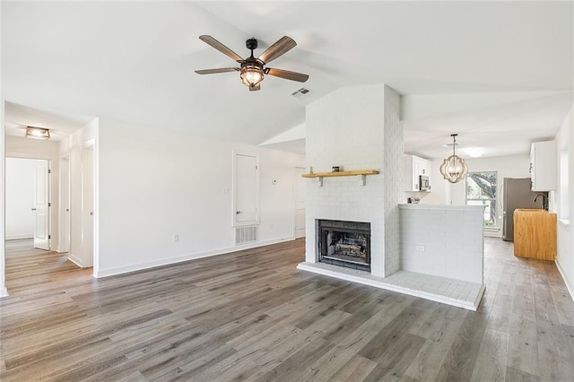 unfurnished living room with lofted ceiling, a brick fireplace, hardwood / wood-style floors, and ceiling fan