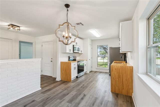 kitchen with white cabinetry, stainless steel appliances, decorative light fixtures, and wooden counters