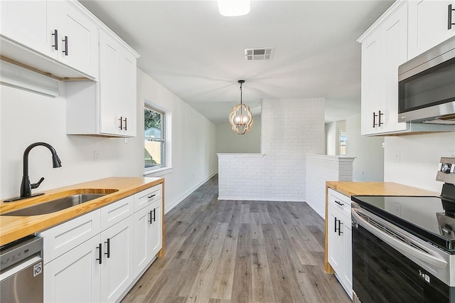 kitchen with stainless steel appliances, sink, white cabinets, and butcher block countertops