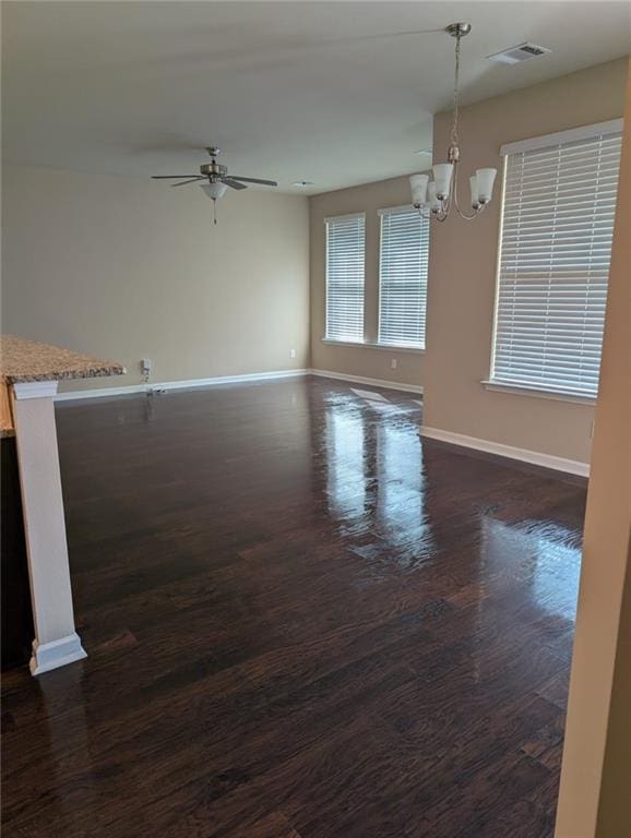 empty room with dark wood-type flooring and ceiling fan with notable chandelier