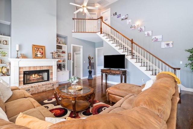 living room with built in shelves, dark wood-type flooring, ceiling fan, a towering ceiling, and a fireplace