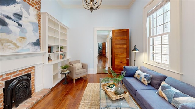 living room featuring crown molding, hardwood / wood-style floors, a brick fireplace, and a notable chandelier