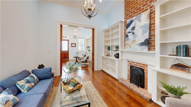 living room featuring built in shelves, an inviting chandelier, light wood-type flooring, ornamental molding, and a fireplace