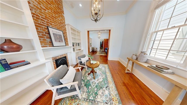 sitting room featuring crown molding, an inviting chandelier, a fireplace, and hardwood / wood-style floors