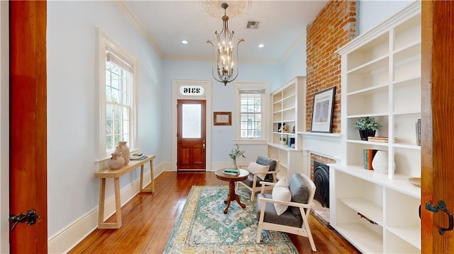 living area with an inviting chandelier, a brick fireplace, hardwood / wood-style flooring, and ornamental molding