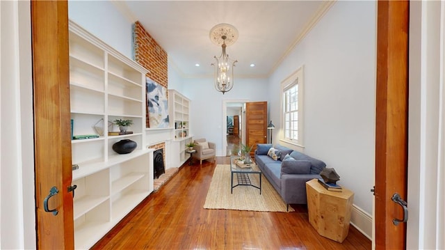 sitting room with an inviting chandelier, ornamental molding, wood-type flooring, and a fireplace