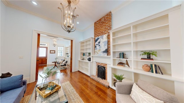 living room with ornamental molding, a brick fireplace, a chandelier, and wood-type flooring