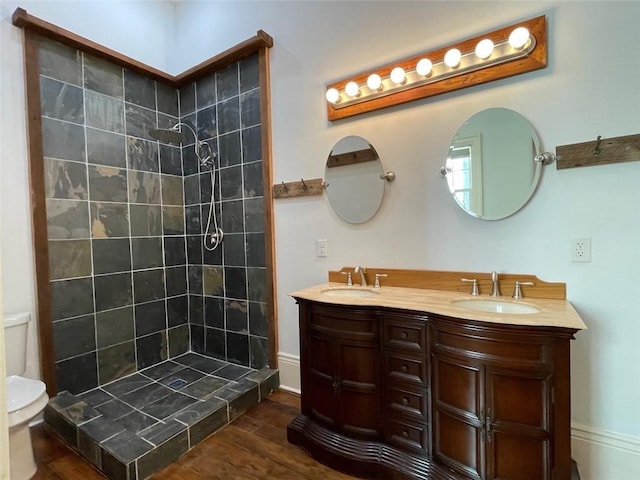 bathroom featuring a tile shower, vanity, wood-type flooring, and toilet