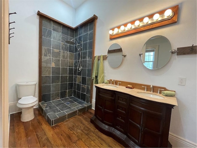 bathroom featuring hardwood / wood-style flooring, vanity, tiled shower, and toilet