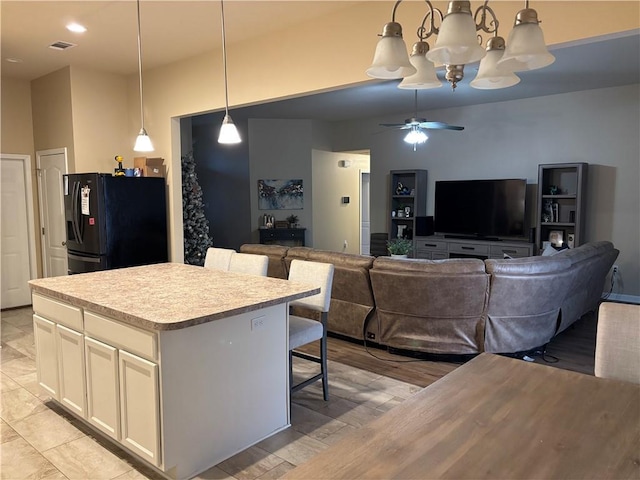 kitchen featuring pendant lighting, white cabinetry, a breakfast bar area, a center island, and black refrigerator with ice dispenser