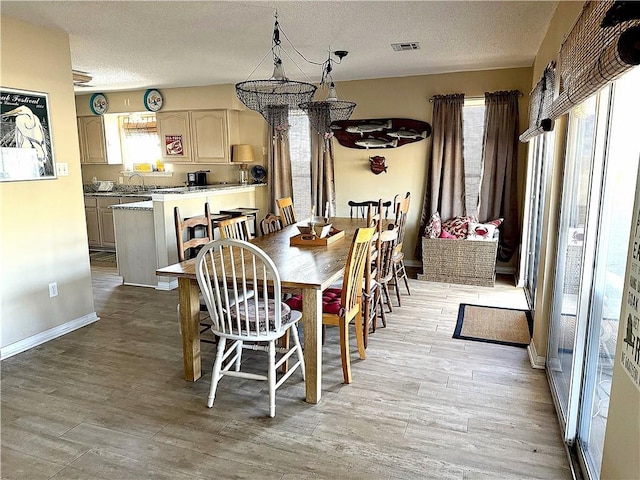 dining space with light wood finished floors, baseboards, visible vents, and a textured ceiling