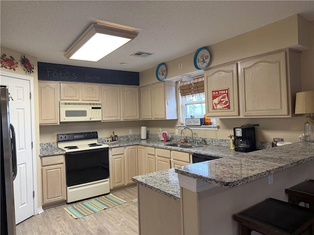 kitchen featuring visible vents, a sink, light stone countertops, white appliances, and a peninsula