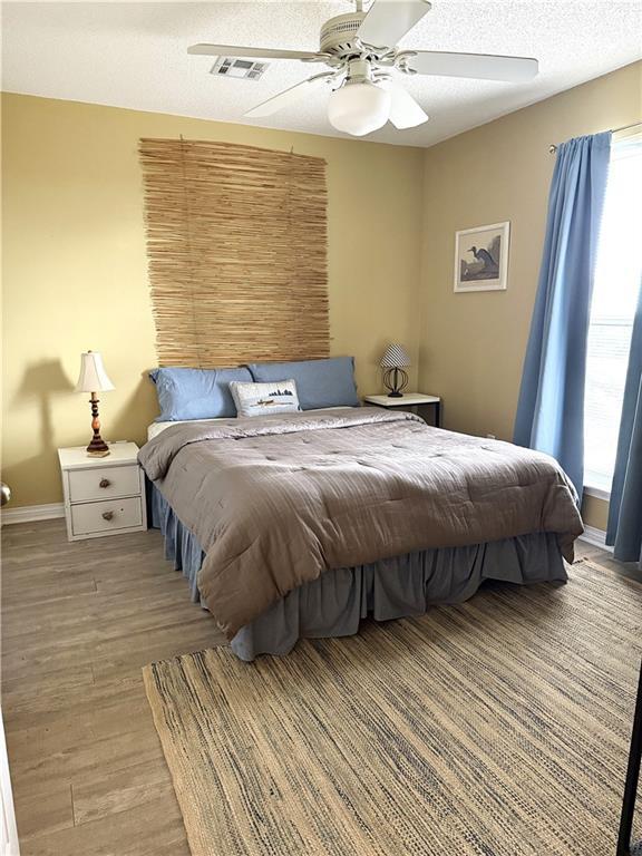 bedroom featuring light wood-type flooring, ceiling fan, a textured ceiling, and baseboards