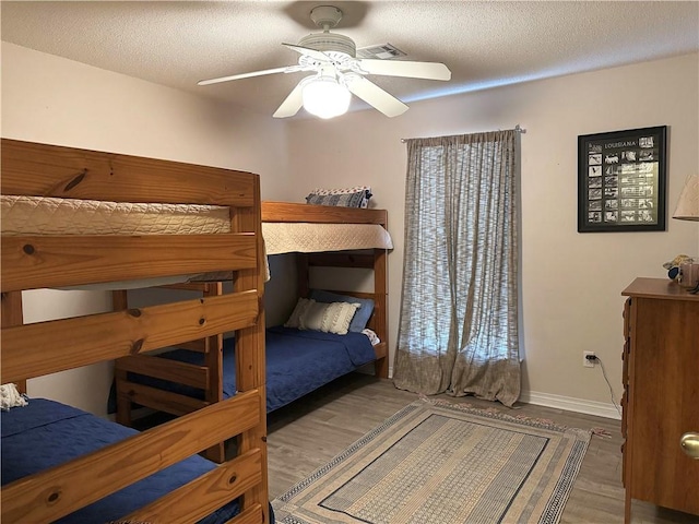 bedroom featuring ceiling fan, a textured ceiling, baseboards, and wood finished floors