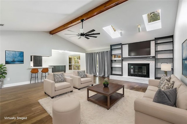 living room featuring a brick fireplace, wood-type flooring, vaulted ceiling with skylight, and ceiling fan