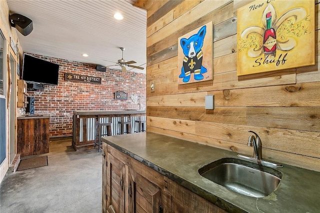 bar featuring sink, ceiling fan, brick wall, and wood walls