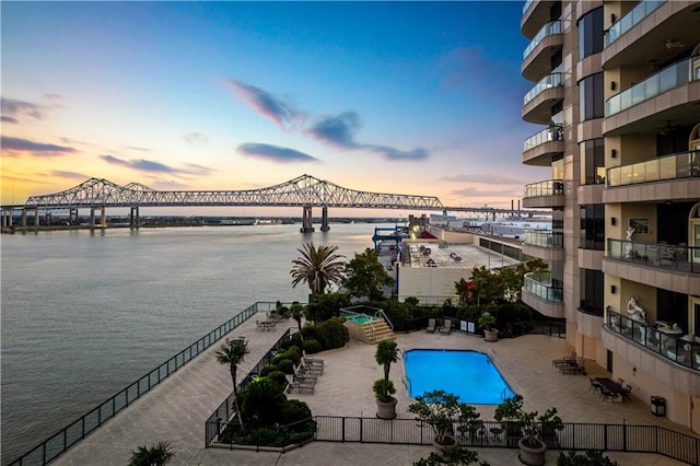 pool at dusk with a patio and a water view