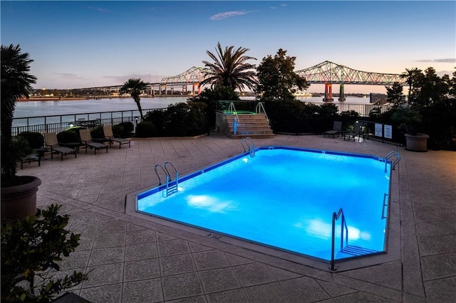 pool at dusk featuring a water view and a patio area