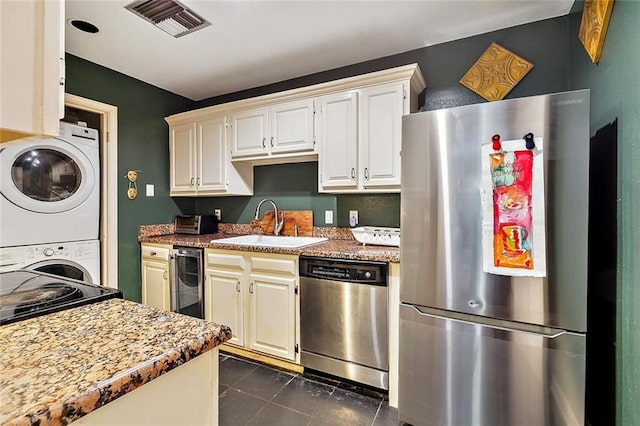 kitchen featuring sink, dark tile patterned floors, stainless steel appliances, stacked washer / drying machine, and light stone countertops