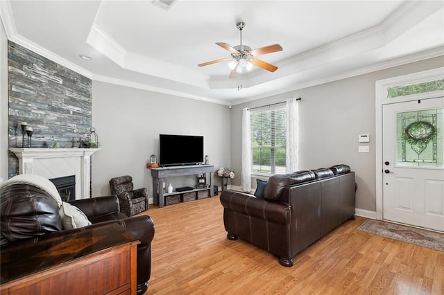 living room with light hardwood / wood-style flooring, ornamental molding, a raised ceiling, ceiling fan, and a fireplace