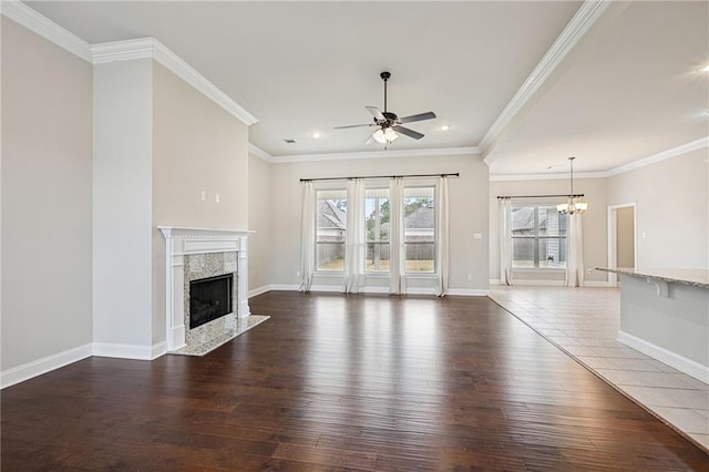 unfurnished living room featuring ornamental molding, dark hardwood / wood-style flooring, ceiling fan with notable chandelier, and a fireplace