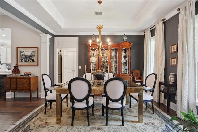 dining space with hardwood / wood-style flooring, a raised ceiling, a chandelier, and ornate columns