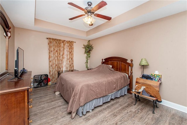 bedroom featuring hardwood / wood-style flooring, ceiling fan, and a raised ceiling