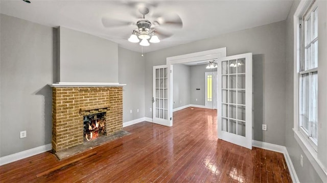 unfurnished living room with a ceiling fan, french doors, a brick fireplace, hardwood / wood-style flooring, and baseboards