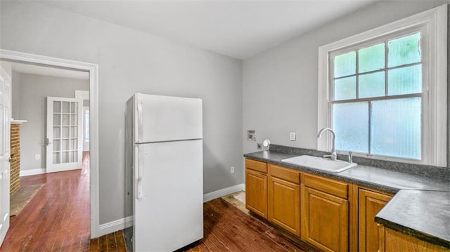 kitchen with brown cabinetry, dark countertops, a sink, freestanding refrigerator, and dark wood-type flooring