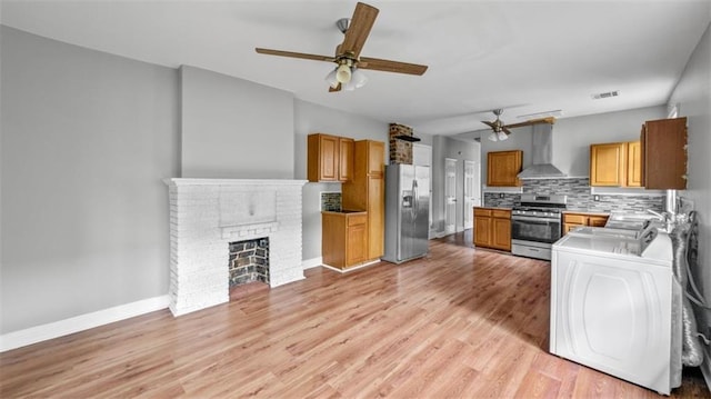 kitchen with appliances with stainless steel finishes, wall chimney exhaust hood, washer / clothes dryer, a ceiling fan, and backsplash