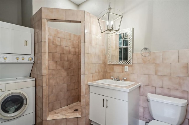 bathroom featuring vanity, stacked washer and dryer, tile walls, a walk in shower, and a notable chandelier