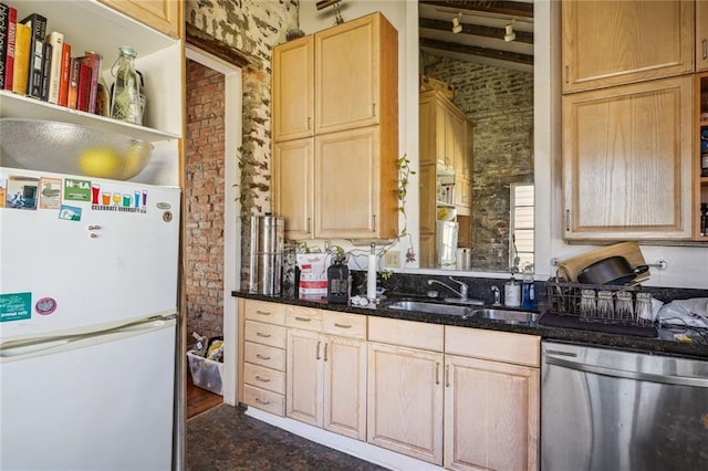 kitchen with a sink, light brown cabinets, brick wall, freestanding refrigerator, and stainless steel dishwasher