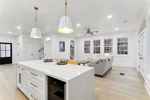 kitchen with wine cooler, built in shelves, a kitchen island, pendant lighting, and white cabinets