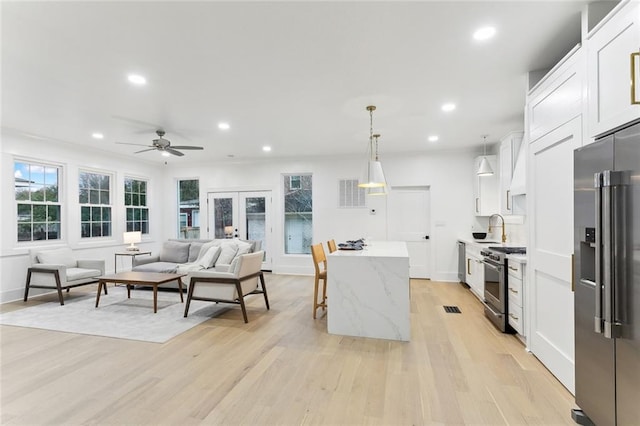 kitchen with decorative light fixtures, white cabinetry, high end appliances, light stone counters, and light hardwood / wood-style flooring