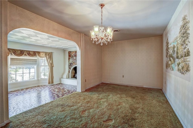 carpeted empty room with an inviting chandelier and a fireplace