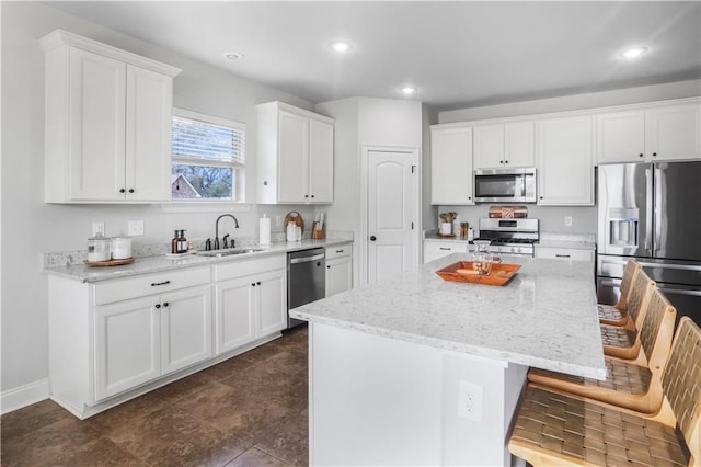 kitchen with sink, white cabinetry, light stone counters, appliances with stainless steel finishes, and a kitchen island