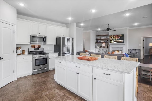 kitchen featuring white cabinetry, crown molding, light stone counters, a center island, and appliances with stainless steel finishes