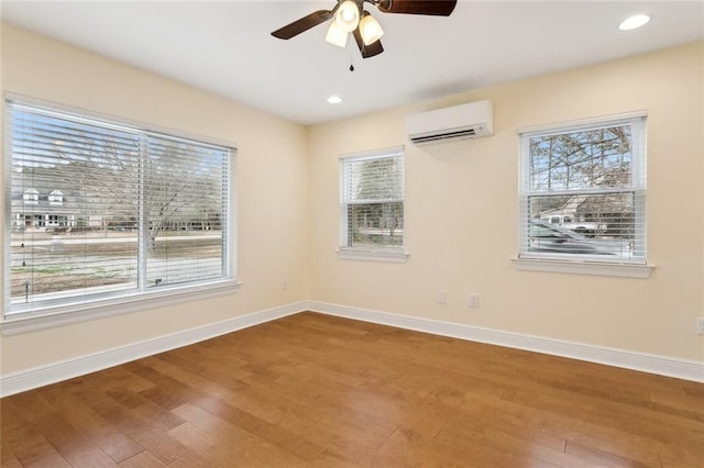 empty room featuring hardwood / wood-style floors, a wall unit AC, a healthy amount of sunlight, and ceiling fan