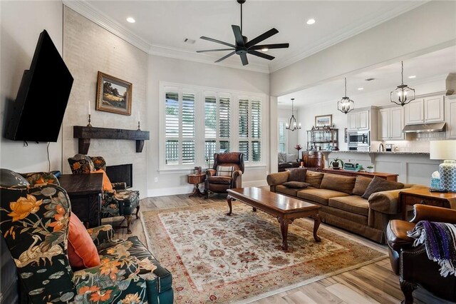 living room featuring crown molding, a large fireplace, ceiling fan with notable chandelier, and light hardwood / wood-style flooring