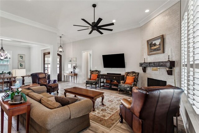 living room with crown molding, a large fireplace, and ceiling fan with notable chandelier