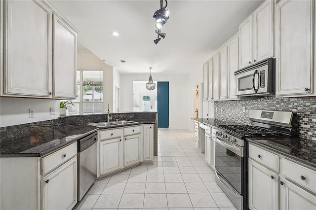 kitchen featuring appliances with stainless steel finishes, sink, dark stone counters, and decorative light fixtures