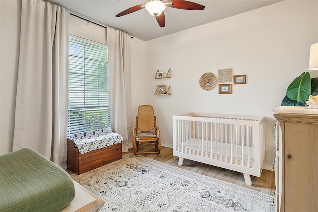 bedroom with multiple windows, light hardwood / wood-style floors, a nursery area, and ceiling fan