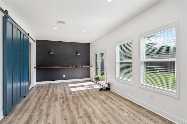 unfurnished room featuring a barn door, a healthy amount of sunlight, and light wood-type flooring