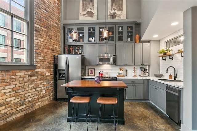 bar featuring sink, stainless steel appliances, tasteful backsplash, brick wall, and decorative light fixtures