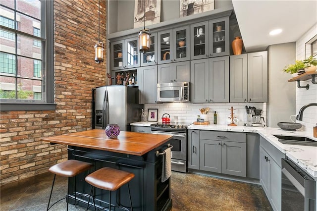 kitchen featuring brick wall, appliances with stainless steel finishes, decorative light fixtures, tasteful backsplash, and sink